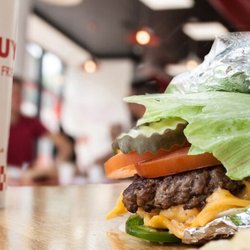 Five Guys - A close-up photograph of a Five Guys cheeseburger with pickles, tomatoes and jalapenos in a lettuce wrap.