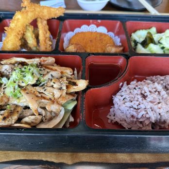 Sushi Pure - Teriyaki Bento - A compartmentalized bento box containing rice, grilled chicken with green onions, tempura vegetables, pickled vegetables, and a fried item, with soy sauce in the center. - Sushi Bars Near Me - Eugene, Oregon