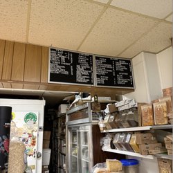Back of the store, showing a spice rack as well as a list of cheeses and olives with their prices.