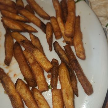 Denny's - Seasoned french fries - A white plate holds seasoned French fries, some darker and more cooked, on a wooden table in a restaurant setting. - Diners Near Me - Mauston, Wisconsin