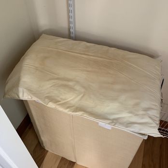 Sandpiper Rentals - A beige mattress with a yellowish pillow on top is positioned in a corner of a room, next to a white wall and a door. - Vacation Rentals Near Me - Edgartown, Massachusetts