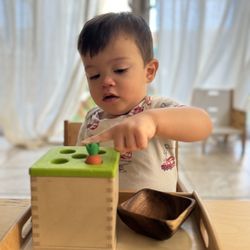 Little Explorers Montessori - Infant exploring object permanence material, developing focus, hand-eye coordination, and early cognitive skills.