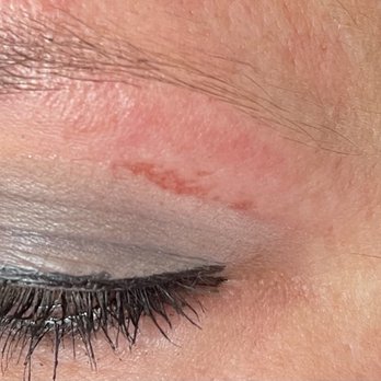 Famous Nails - The image shows a close-up of a person's closed eye, highlighting the eyelid with makeup, including eyeliner and eyeshadow. The skin around the eye displays natural texture and a small scar or mark on the eyelid. Fine eyelashes are visible, and the skin tone appears even with some natural variations. - Nail Salons Near Me - Albuquerque, New Mexico