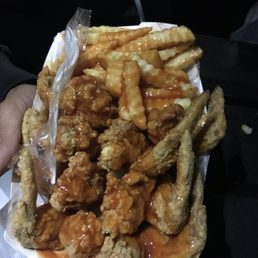 a hand holding a basket of chicken wings and fries
