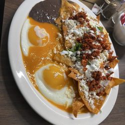 Authentic chilaquiles topped with chorizo, queso fresco, crema, and fresh cilantro, served with sunny-side-up eggs and refried black beans.
