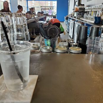 Voodoo Brewing - Inside a coffee shop, a drink with ice and a straw is placed on the counter, with barista tools and jars nearby. Customers and staff are visible in the background. - Brewpubs Near Me - Salisbury, Maryland