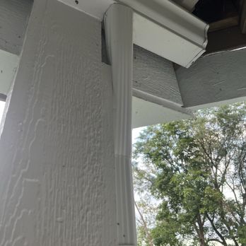 Elite Exteriors - A white gutter and downspout are attached to the corner of a house with light-colored siding, with trees visible in the background. - Roofing Near Me - New Berlin, Wisconsin