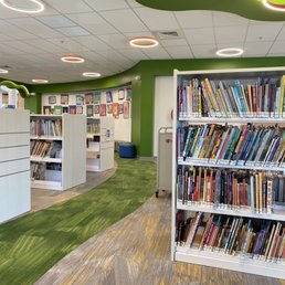 Interior of a library with bookshelves filled with books, green and white walls, and a colorful carpeted floor.