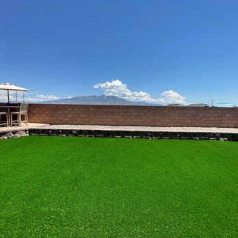 AMG Landscape - Block wall for the planter area and raised patio. - A rooftop patio features artificial grass, a brick wall, and a table with chairs and an umbrella, with mountains and clouds in the background. - Irrigation Near Me