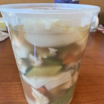 Lucky Wok - Bowl of wor wonton soup - A transparent plastic container holds wonton soup with visible dumplings and vegetables, placed on a wooden surface. - Chinese Near Me - Albuquerque, New Mexico