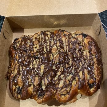Harrison Bake Shop - a pastry in a box - A large pastry with chocolate chips and cookie crumble topping, drizzled with chocolate, in a brown takeout box. - Bakeries Near Me - Harrison, New York