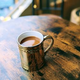 Bourbon coffee - A ceramic mug filled with coffee sits on a rustic wooden table, with a blurred background suggesting a cafe environment.