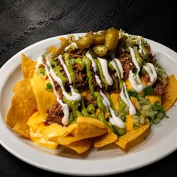 Crispy tortilla chips loaded with rich nacho cheese, tender birria, creamy sour cream, fresh guacamole, diced onion, cilantro, and jalapeños