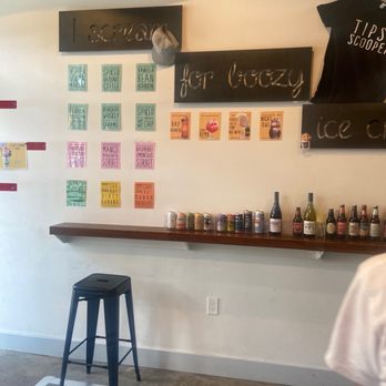 Tipsy Scoop - A wall displays colorful menu signs and a shelf with canned beverages and bottles at Tipsy Scoop ice cream shop. - Ice Cream & Frozen Yogurt Near Me - Brooklyn, New York