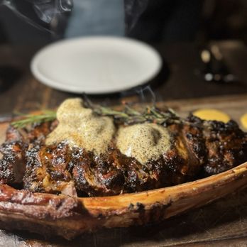 Platea - A steak dish with herb and peppercorn sauce is presented on a wooden platter, with a sprig of herbs and a small bowl of sauce nearby. - Peruvian Near Me - Pinecrest, Florida