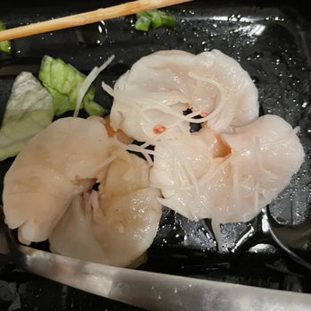 Paste Thai - Undercooked shrimp from spring roll - Cooked scallops with shredded cheese and chopped green onions are placed on a black plate, with a pair of tongs and chopsticks nearby. - Thai Near Me - Davis, California