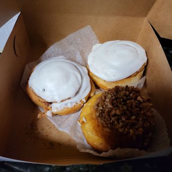 Allegretti's Bakery - Three donuts inside a brown bakery box, two with white icing and one topped with chopped nuts, on a dark surface. - Bakeries Near Me - Norridge, Illinois