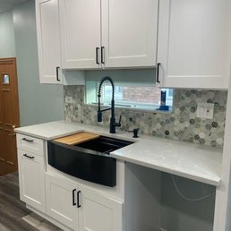 A kitchen setup featuring white cabinetry, a black farmhouse sink, and a mosaic tile backsplash with hexagonal patterns.