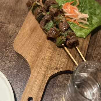 Quan Pho - Beef skewer with veggies - Two beef and vegetable skewers are placed on a wooden serving board, accompanied by lettuce and shredded carrots. - Vietnamese Near Me - Saugus, Massachusetts