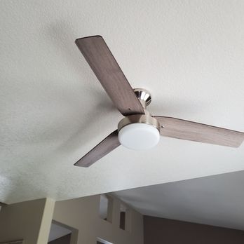 John Belanger Construction - Ceiling fans install at a reasonable price - A ceiling fan with three wooden blades and a central light fixture is mounted on a white ceiling in an indoor space. - Handyman Near Me - Corona, California