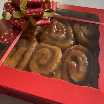 The General Store - Sticky buns - A red gift box with a transparent window displays cinnamon rolls with icing, decorated with a red and gold star-patterned bow. - Bakeries Near Me - Carleton Place, Ontario