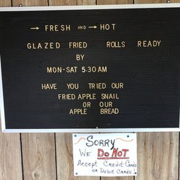 Cash only please - The image shows a black letter board mounted on a wooden wall, listing menu items such as glazed fried rolls, fried apple snail, and apple bread, with business hours from Monday to Saturday at 5:30 AM. Below, a handwritten sign on white paper indicates that credit and debit cards are not accepted, apologizing for the inconvenience.