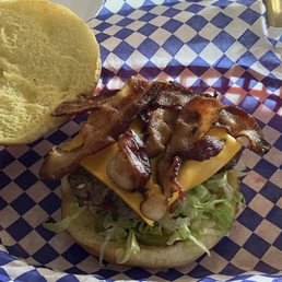 Bacon Cheeseburger - A bacon cheeseburger features crispy bacon strips, a slice of melted cheese, shredded lettuce, and a sandwich bun, placed on checkered paper in a basket. The burger is assembled with fresh ingredients and presented in a casual setting.