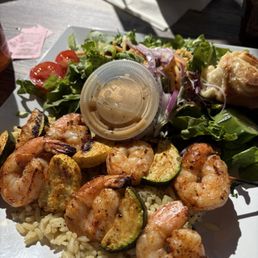 Grilled shrimp and veggies over seasoned rice, with side salad and an orange roll.