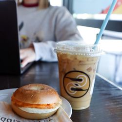 A close-up of a Ziggi's iced coffee and breakfast sandwich sitting on a café table, creating a casual coffee-shop breakfast scene.