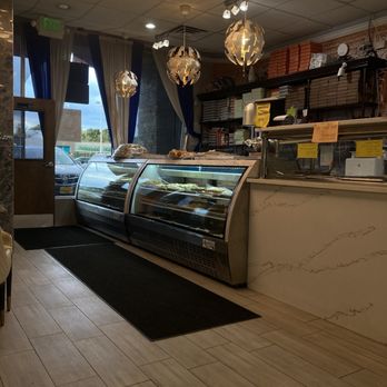 Dera - dessert choices - A bakery or cafe interior featuring glass display cases with baked goods, bookshelves with items, and decorative pendant lights. - Pakistani Near Me - Springfield, Virginia