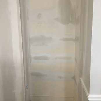 Reliable Drywall - Finished worksite. - The image shows an interior wall that appears to be in the process of painting or priming, with uneven patches of primer or paint visible. The wall is next to a corner with a baseboard at the bottom, and the floor is made of wood or laminate planks. The wall's surface is unpainted or partially painted, indicating ongoing renovation or preparation work. - Drywall Installation & Repair Near Me - Willow Grove, Pennsylvania
