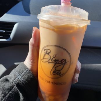 Bing Tea - Thai Tea with fresh handmade boba - A person holds a large iced boba tea in a clear cup with a pink heart-shaped straw, inside a vehicle. - Desserts Near Me - Albuquerque, New Mexico