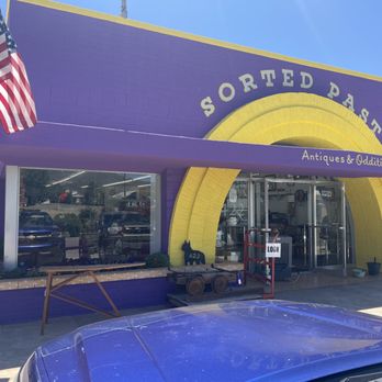Sorted Past - Front - Sorted Past, an antiques and oddities store, features a purple exterior with yellow accents and a large sign. An American flag is displayed outside, and the entrance has glass doors with an 'Open' sign. - Used, Vintage & Consignment Near Me - Bisbee, Arizona