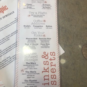 Cafe Olympic - Deserts - The menu from Olympic restaurant displays a list of drink options including mimosas, coffee add-ons, and house-infused Bloody Marys. It features sections for mimosas on tap, coffee additives, and house Bloody Mary varieties, with prices ranging from $1 to $10. The menu is printed on white paper with red and black text, and includes descriptions of each drink. The menu is placed on a table with a textured surface, and part of another paper is visible underneath. - New American Near Me - Crystal Lake, Illinois