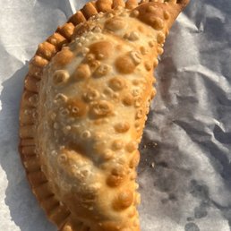Pastelitos - A fried pastry with a bubbly, golden-brown surface rests on crinkled paper, likely a savory or sweet snack from a food truck or street vendor.