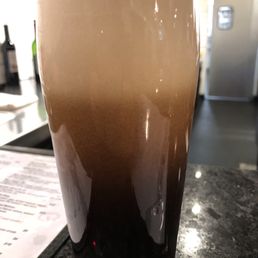 Cask Smoked Schwartzbier (Rauchbier) - A tall, clear glass filled with dark beer and topped with a thick foam head, placed on a bar counter with a menu nearby.