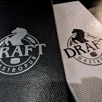 Draft Gastropub - Two menus from Draft Gastropub are shown, one black and one gray, both with a textured surface. Each menu displays a logo with a horse silhouette and the word "DRAFT" in large letters, along with the words "GASTROPUB" underneath. The menus are positioned at an angle on a dark, reflective surface, highlighting their design and branding. - Gastropubs Near Me - Appleton, Wisconsin