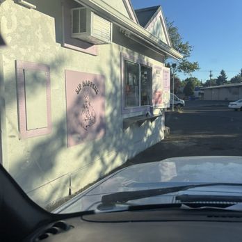 Sip Happens - Window - A small food stand with a pink sign reading 'Slip Happens' and a menu is visible through a window, with shadows cast on the building exterior. - Coffee & Tea Near Me - Eugene, Oregon