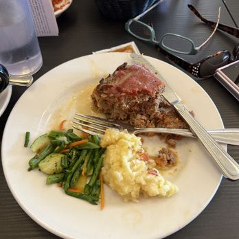 Joe's Dining - A white plate holds a slice of meatloaf, mashed potatoes, and mixed vegetables, with utensils on the plate, on a dark restaurant table. - Pizza Near Me - Santa Fe, New Mexico
