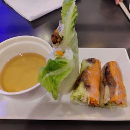 Pork Spring Rolls - Two spring rolls with visible vegetables and meat are placed on a white plate, accompanied by a small bowl of dipping sauce.