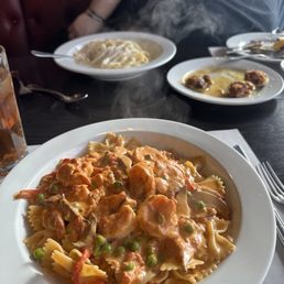 Baked Clams - A dish of shrimp and pasta with green peas in a creamy sauce is on a white plate at a restaurant table.