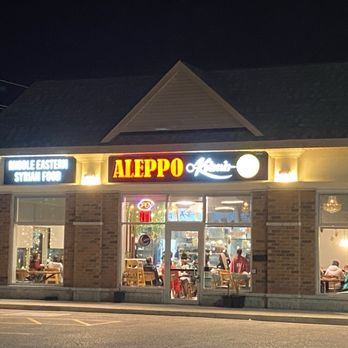 Aleppo Kebab - The restaurant - Night view of Aleppo Kebab restaurant with illuminated signage, visible interior dining area, and customers inside. - Salad Near Me - Ajax, Ontario