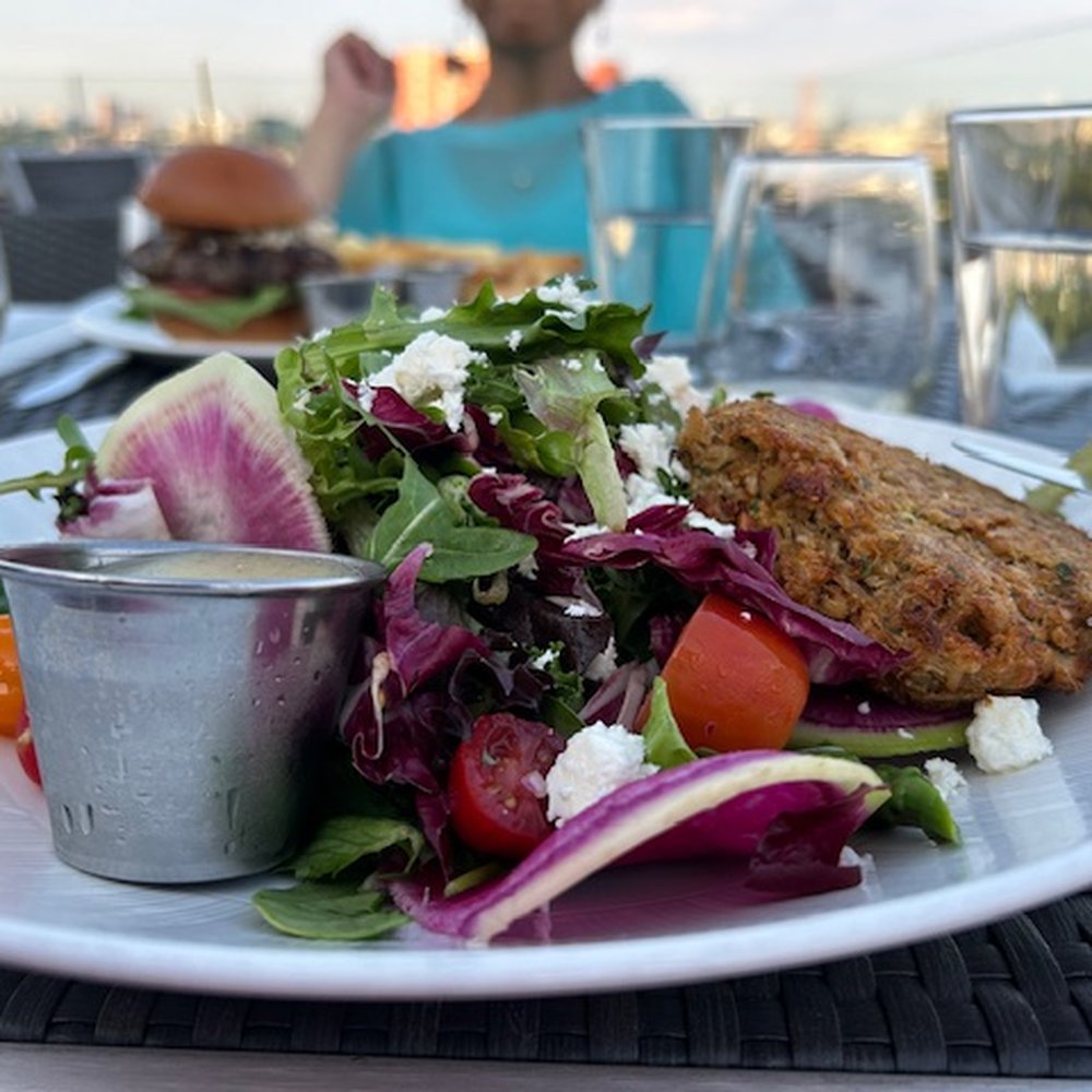 Over The Charles Rooftop Bar - Mixed green salad with vinaigrette dressing on side and a crabcake. - Tapas/Small Plates Near Me - Boston, Massachusetts Over The Charles Rooftop Bar - Mixed green salad with vinaigrette dressing on side and a crabcake. - Tapas/Small Plates Near Me - Boston, Massachusetts