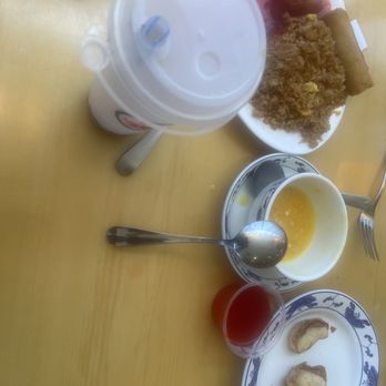 Royal Dragon - Good left by 2 hungry hungry people and it was so good!!!! Time to take this home! - The image shows a table with a variety of Asian dishes and beverages. There is a plate with fried rice, spring rolls, and skewered meat. A large drink with a straw is positioned at the top, and a bowl with a yellow liquid and a spoon is in the center. A small glass with red liquid and a plate with fried items are also visible. The table surface is light-colored wood, and utensils are placed around the dishes. - Chinese Near Me - Roy, Utah