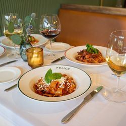 Felice West Palm Beach - A spread of Italian cuisine featuring rigatoni, spaghetti, and various pasta bowls. The table is set with glasses of red and ...