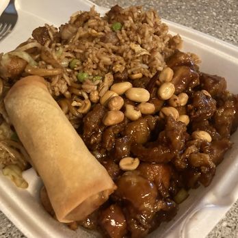 Golden Star - 3. Kung Pao Chicken Combo Plate with 2. Pot Sticker - A foam takeout container contains fried rice, stir-fried noodles, a spring roll, and chicken topped with peanuts, served on a gray countertop. - Chinese Near Me - Redding, California