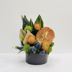 Urban Flowers Chicago - A bold, sculptural arrangement inspired by the rich colors and textures of the tropics. Vibrant orange anthurium and pincushion protea
