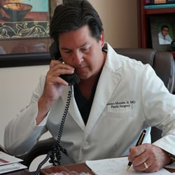 The Plastic Surgeon Miami - Dr. Ramiro Morales in his office answering patient inquiries.