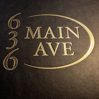 636 Main Ave - A photograph features a black textured menu cover with gold embossed lettering. The text includes the address '636 Main Ave' arranged vertically on the left side and 'Main Ave' inside an oval shape on the right. The design is simple and elegant, indicating it is likely from a restaurant or similar establishment located at that address. - New American Near Me - Durango, Colorado