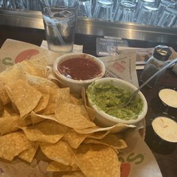 Chips, Guacamole, Salsa and Ranch - A plate of tortilla chips served with bowls of salsa, guacamole, and ranch dressing, with a glass of water and a salt shaker on a restaurant table.